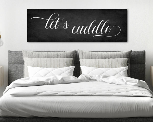 Let's Cuddle' canvas in a charcoal background above headboard in romantic bedroom setting.