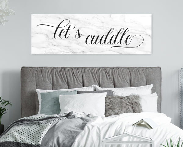 Let's Cuddle' canvas in a marble background above headboard in romantic bedroom setting.