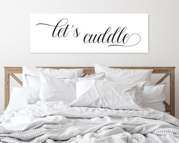 Let's Cuddle' canvas in a white background above headboard in romantic bedroom setting.