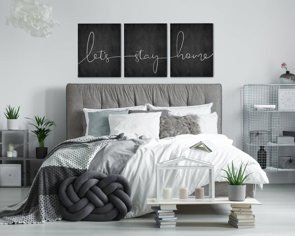 Let’s Stay Home 3-piece canvas wall art set hanging above a bed.