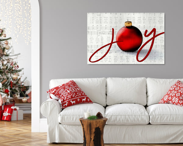 Joy to the World Christmas canvas with elegant script, ornament, and vintage sheet music background in a silver color on a wall with a Christmas Tree. 